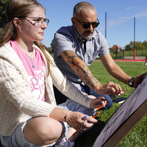 A professor ourtside with a student creating art