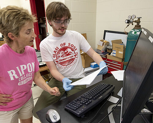 A professor leans in and looks at a students progress