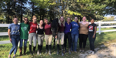 10 female Ripon College students pose outdoors with horse