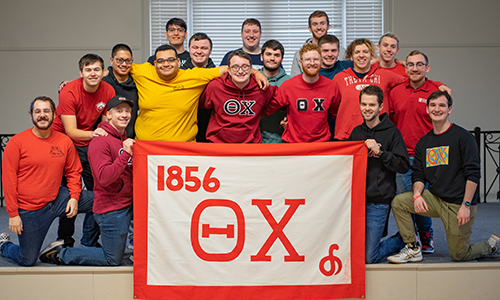 Ripon College Theta Chi fraternity members take a group picture with the fraternity's banner