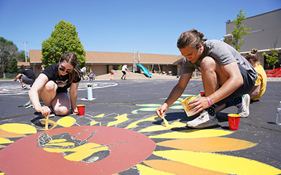 Two students paint a playground mural as a community service project