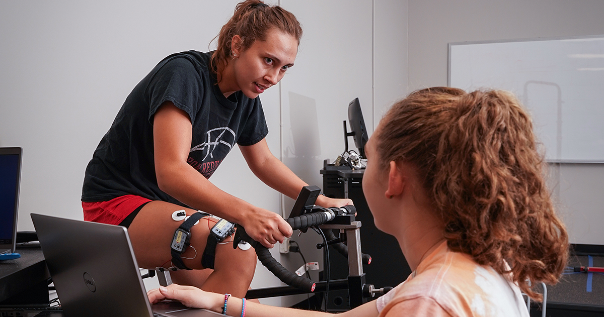 Macy Goldthorpe '26 conducts research gauging muscle activity while Kassidy Walters '23 rides a stationary bike