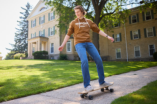 A student longboards down the path from the Quad residence halls
