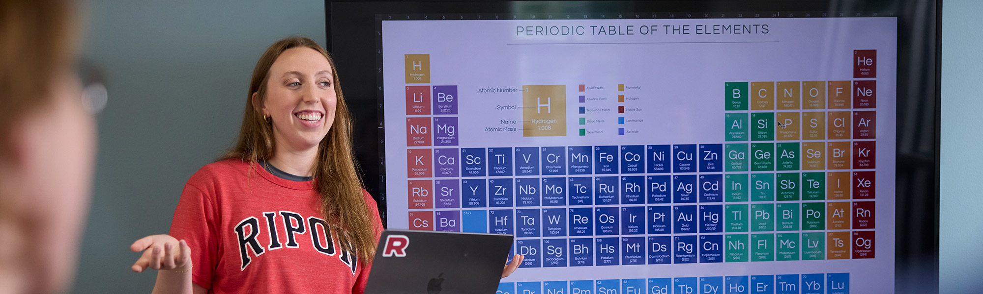 A student stands in front of the periodic table of elements