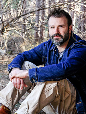 Author sits in front of a forest