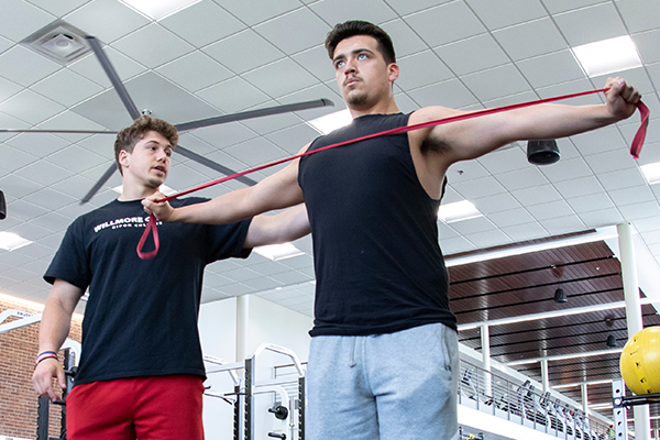 A student coaches another student while stretching