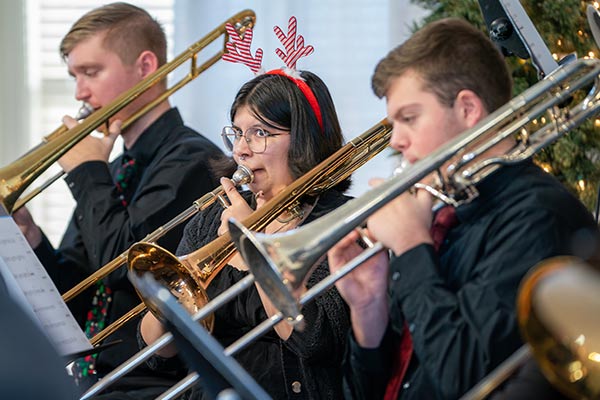 Three trombone players playing Holiday songs in Great Hall. One in fun reindeer ears.