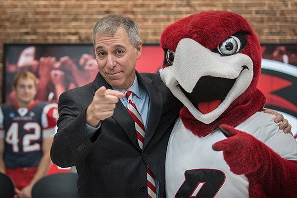 President Messitte and Rally the Red Hawk point to the camera at the Willmore Center