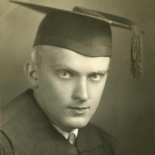 A man in a graduation cap stares intensely
