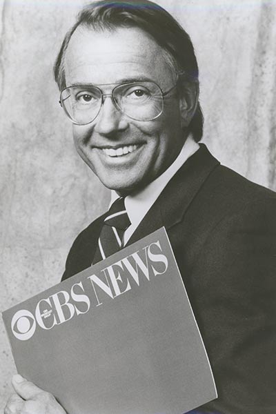 Threlkeld holds a CBS news folder and smiles