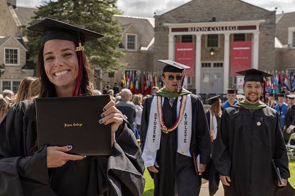 A woman walking in front of two men holding their diploma