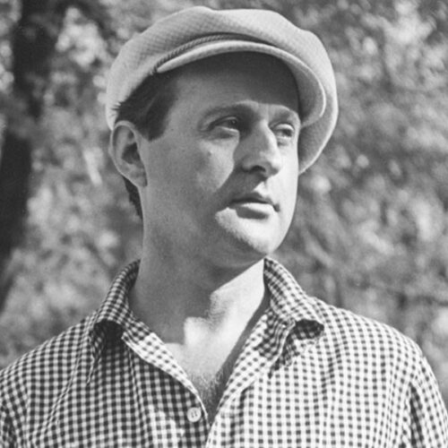 Lester stands in a forested area in a neat hat