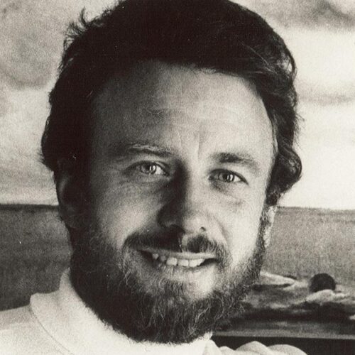 A man in a turtleneck stands in front of the sea