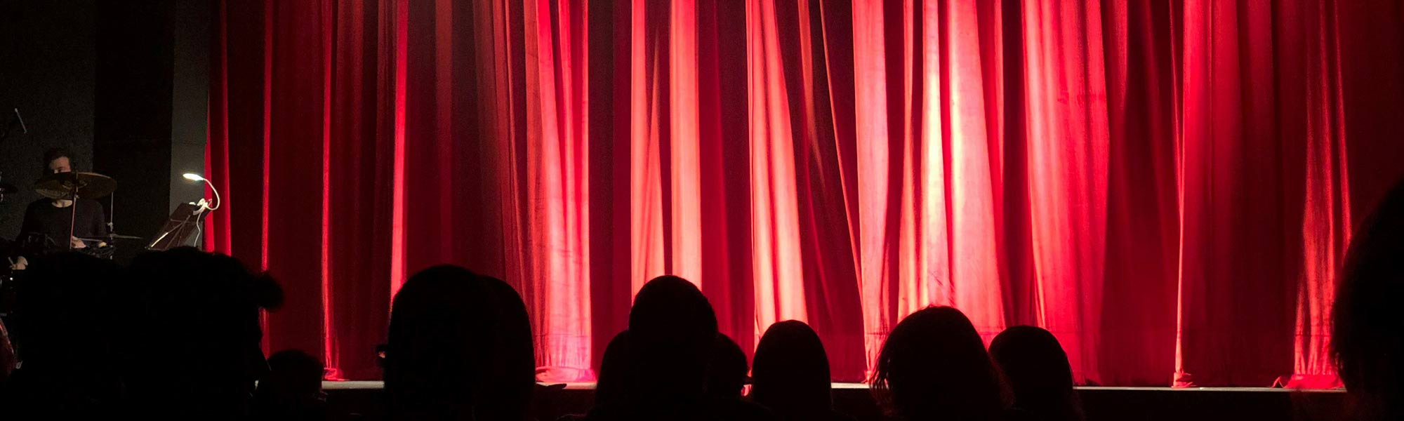 A theatre with a bright red curtain Photo by Monica Silvestre: https://www.pexels.com/photo/people-at-theater-713149/