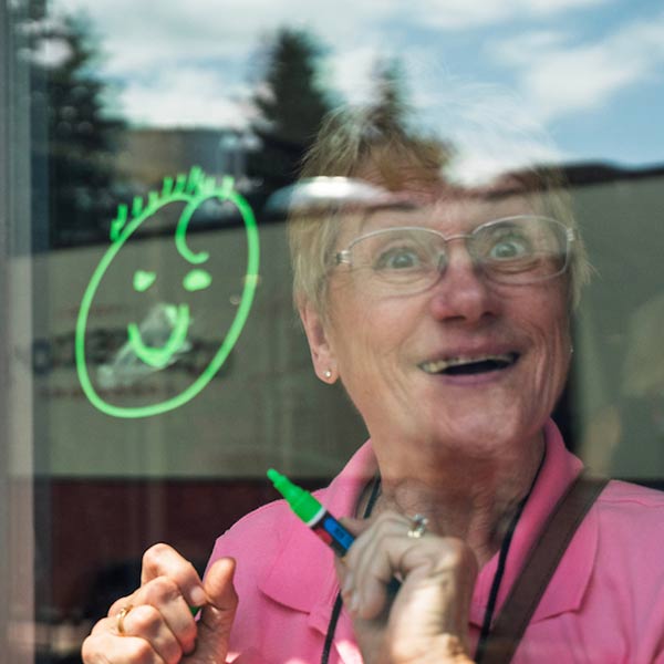 An alumni draws a smiley face on a window and smiles to the camera