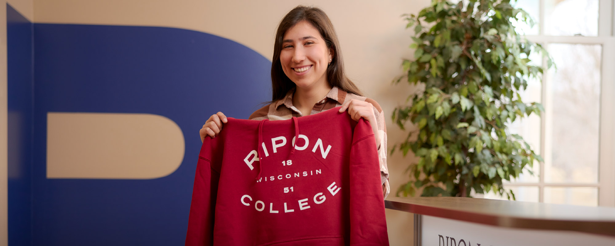 A newly accepted student holds a hoodie in Evans Admissions office.
