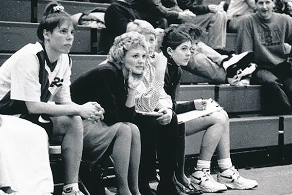 A coach sits next to her players on the court.