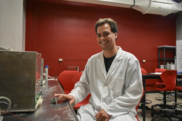 A student in a lab coat smiles at the camera