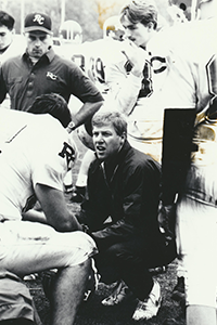 A football coach kneels down and talks to player