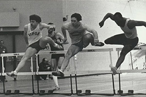 Three men jump over hurdles in a track meet.