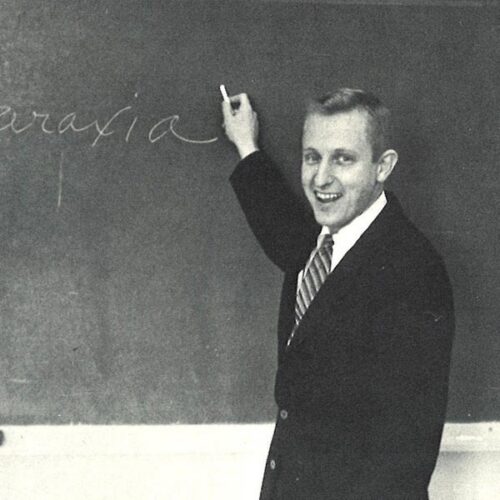 Professor Hannaford with a big smile by a chalkboard.