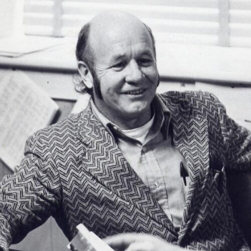 Jerry in a suit smiles while talking to student