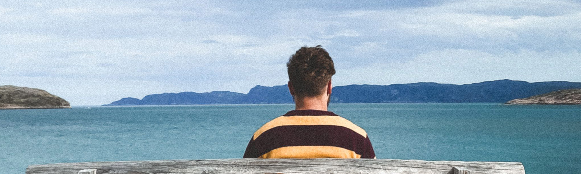 A person sitting on a bench facing a large body of water-Photo-by-Dmitrii-Donskik